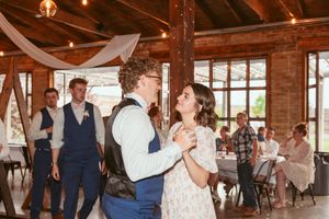 Wedding guests dance together in a rustic barn venue with wooden beams and natural lighting.