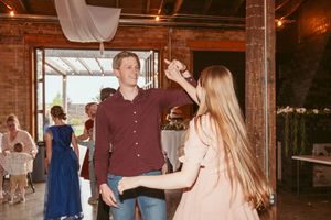 Wedding guests dancing and having fun at a reception in a brick-walled venue.