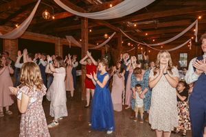 Wedding reception dance party in a rustic barn venue with string lights and white fabric draped from wooden beams.