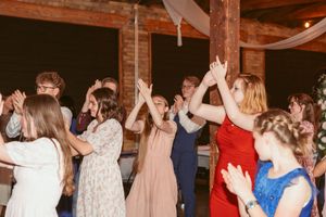 Wedding guests dancing and celebrating on the dance floor at a reception with exposed brick walls and white draping decor.
