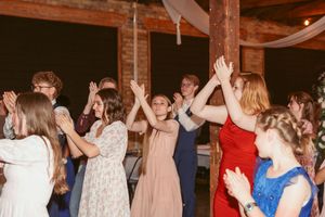 Wedding guests dancing and celebrating with raised hands in a venue decorated with string lights.