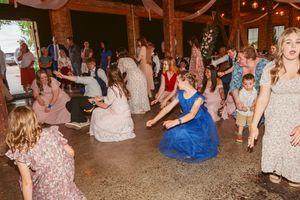 Crowd of wedding guests dancing and celebrating on a wooden floor at a rustic reception venue.