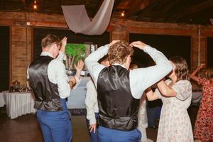 Couples dancing together during an energetic reception celebration in a rustic venue with brick walls.