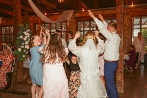 Guests dancing and celebrating at a wedding reception in a rustic brick venue with white drapes.