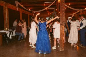 People dancing at a rustic indoor wedding reception venue with wooden beams and string lights overhead.