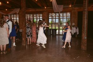 Wedding guests dance and gather in a rustic wooden barn venue with exposed beams and warm lighting.