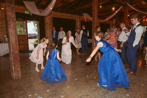 Wedding reception guests dance together on a rustic wooden floor decorated with white drapes in a barn venue.