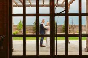 View through wooden window panes of a couple embracing on an outdoor terrace with garden scenery beyond.