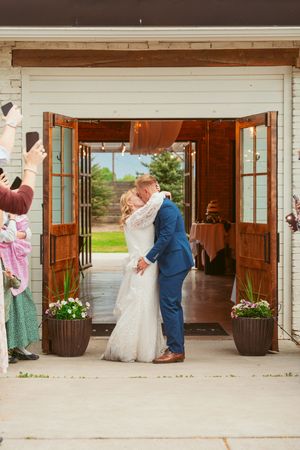 Newlyweds share their first kiss in a rustic doorway decorated with potted flowers.