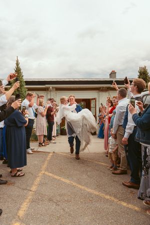 Wedding guests form a receiving line outside a venue on an overcast day with bride and groom walking through.