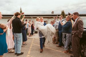 Wedding guests stand in a line outdoors at a reception venue under cloudy skies.