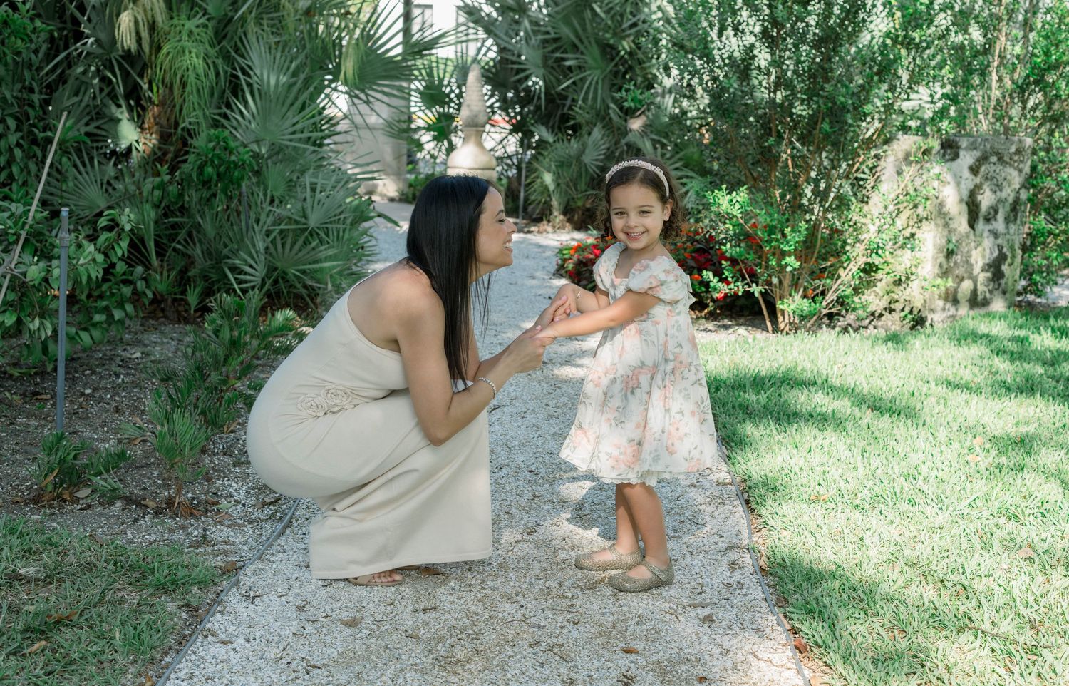 A tender mother-daughter moment captured on a garden path surrounded by tropical greenery.