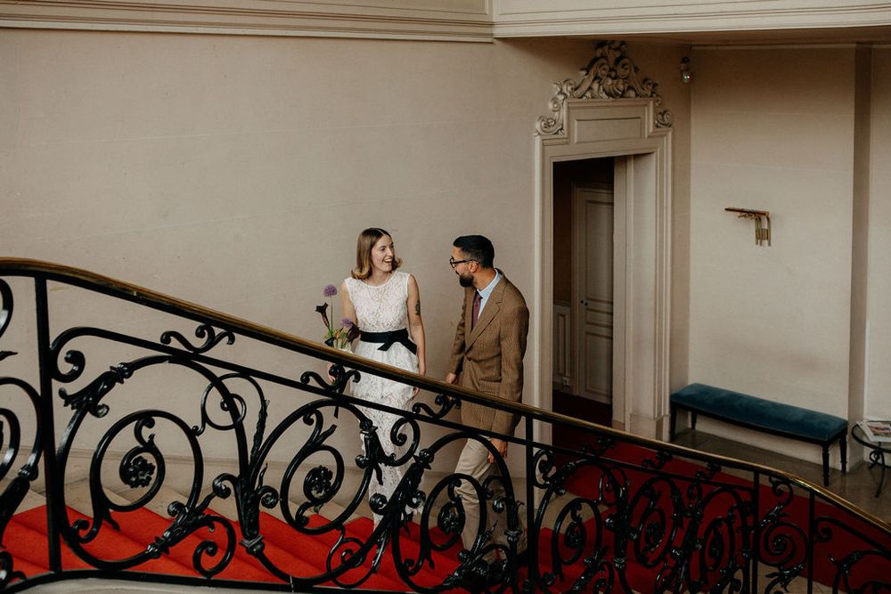Bride and groom share a romantic moment on an ornate staircase with red carpet.