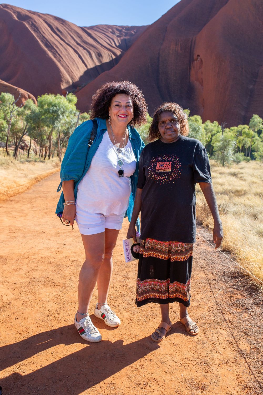 Two people smiling and posing together in front of Uluru's red rocks in the Australian outback.