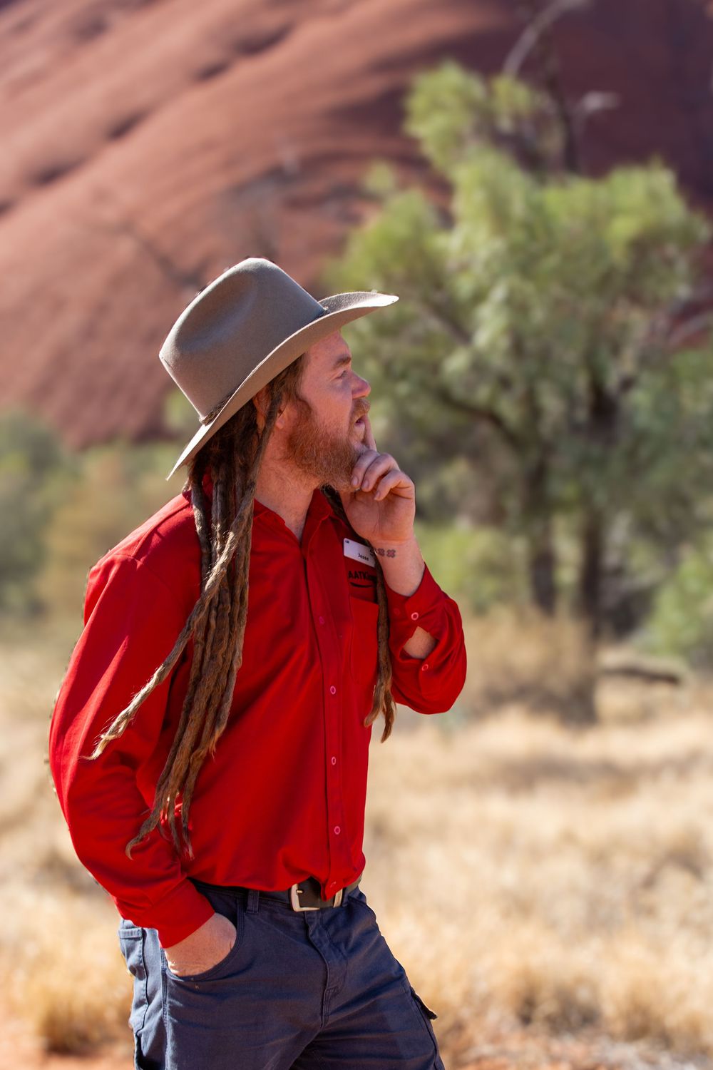 Person in red western shirt and cowboy hat poses outdoors against desert landscape with red rock formations.