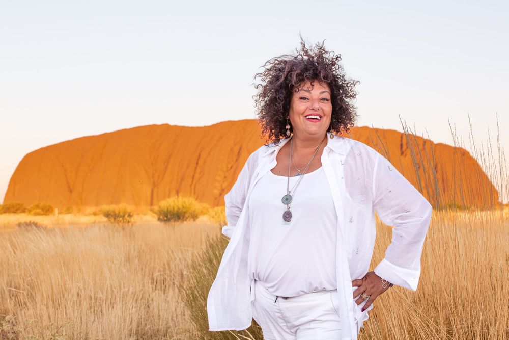 A joyful senior woman wearing white stands gracefully in a golden sunlit field during sunset.