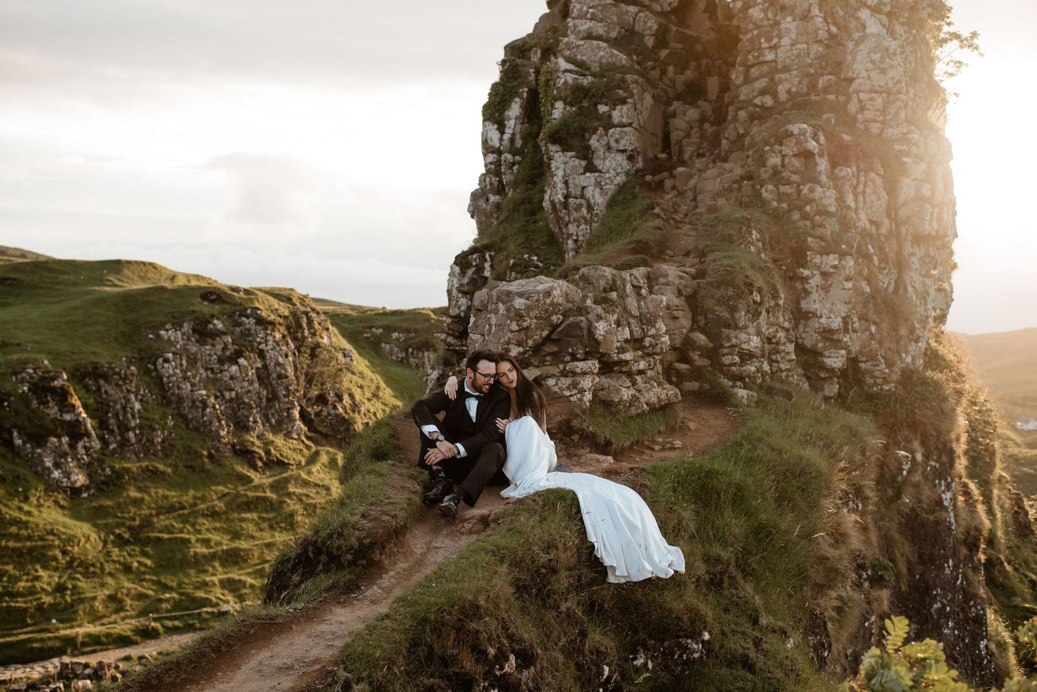 A couple sitting on a destination elopement wedding in Switzerland during golden hour at sunset with dramatic rocky coastal landscape views.