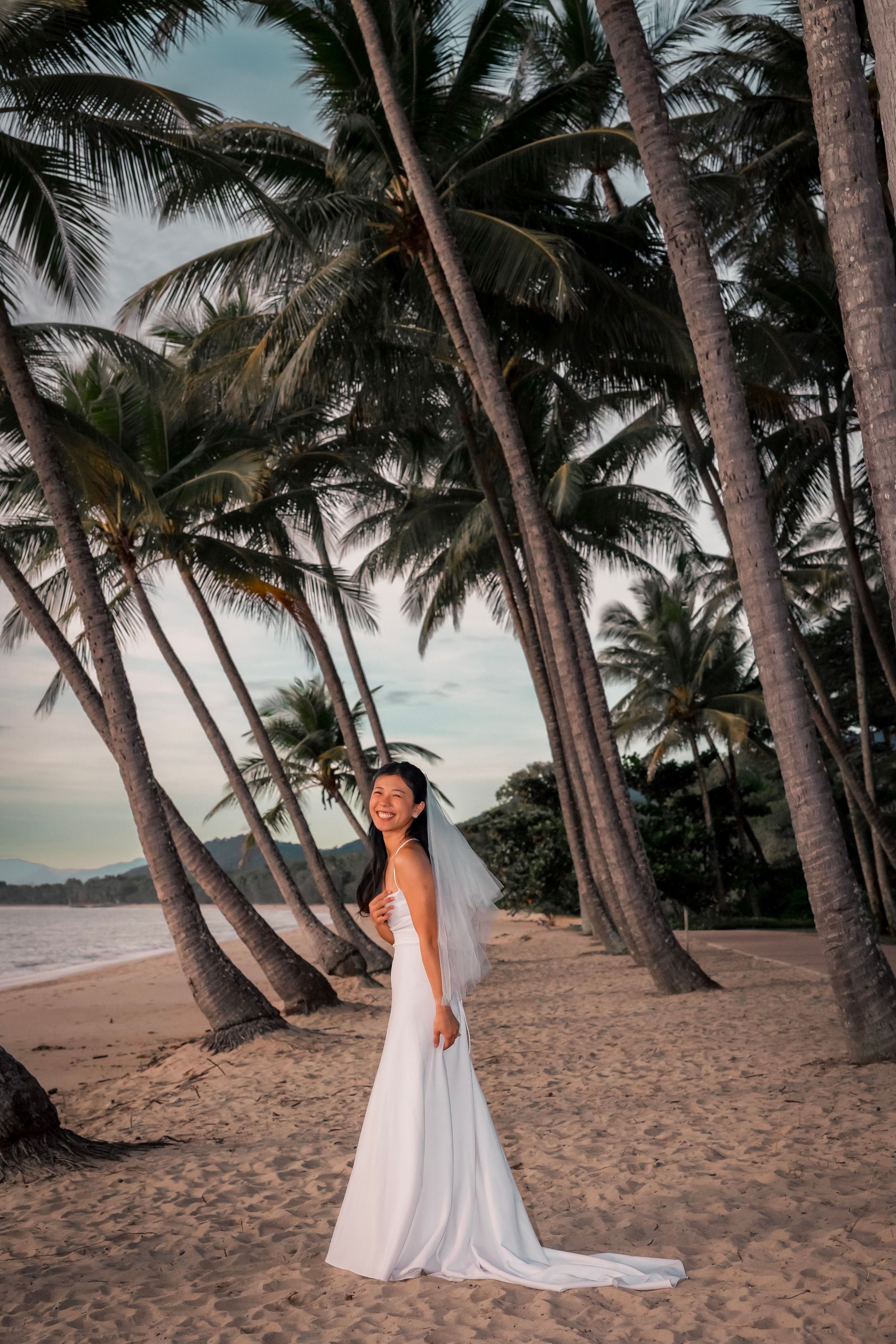 A white flowy dress on a sandy beach with tall palm trees swaying in the tropical sunset light.