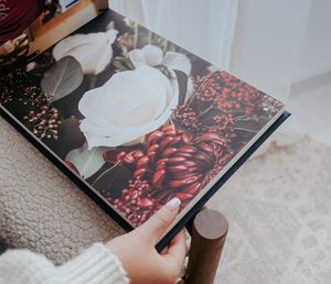 Someone flips through a photography book showing floral images and white roses on a red background.