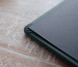 Close-up macro shot of a black leather portfolio corner on a weathered white wooden surface.