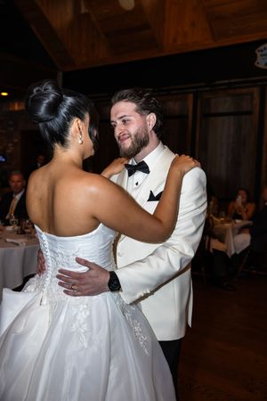 A newlywed couple shares their first dance in an elegant ballroom setting with a rustic wooden backdrop.