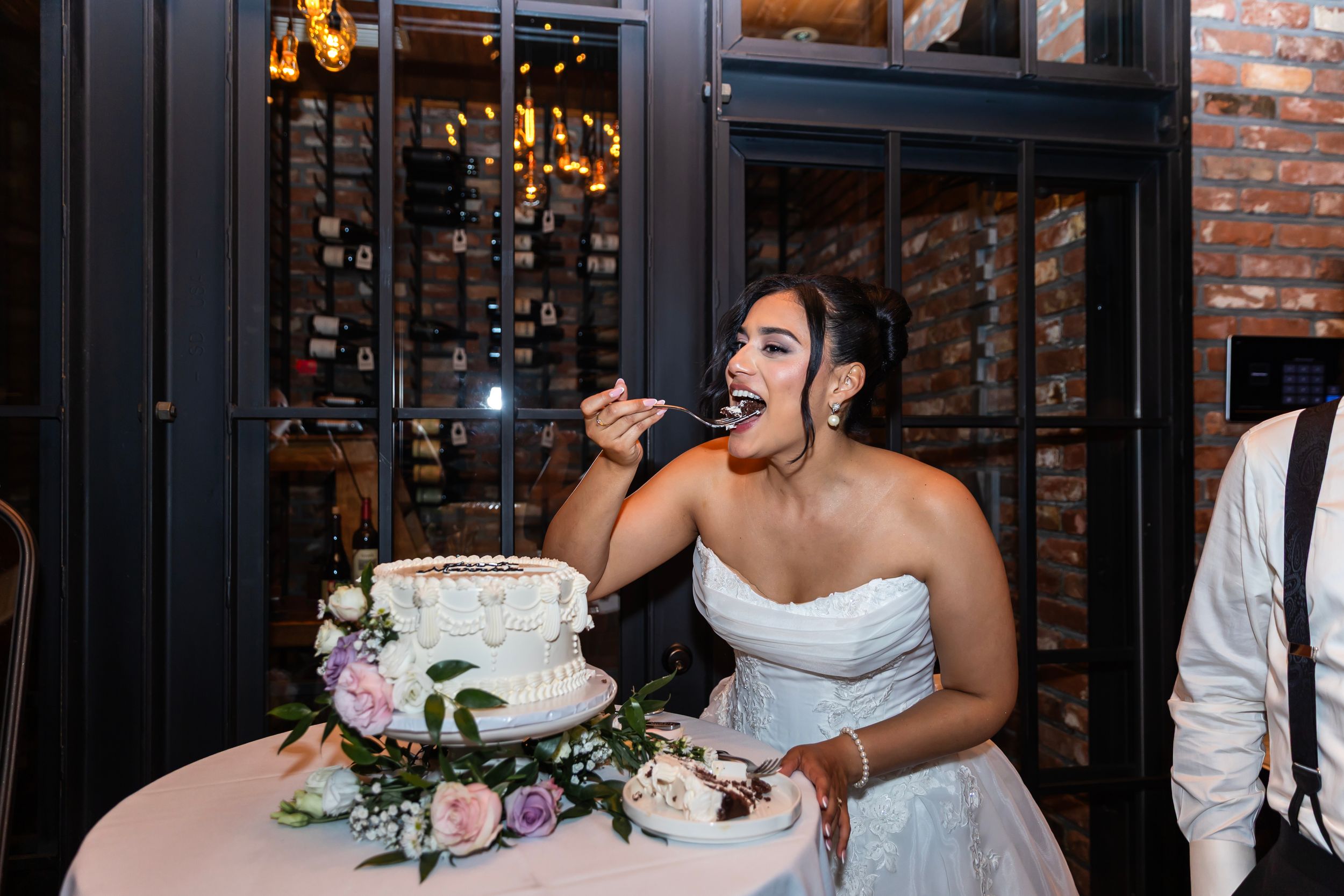 Wedding reception guests raise glasses in a toast at an elegant venue with exposed brick walls and chandeliers.