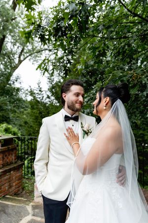 A couple shares an intimate moment during their outdoor wedding ceremony under lush green trees.