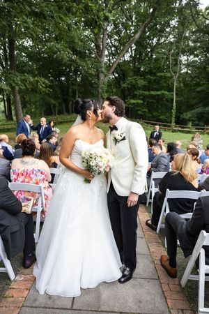 A wedding couple shares a tender moment during their outdoor garden ceremony with guests seated on white chairs.