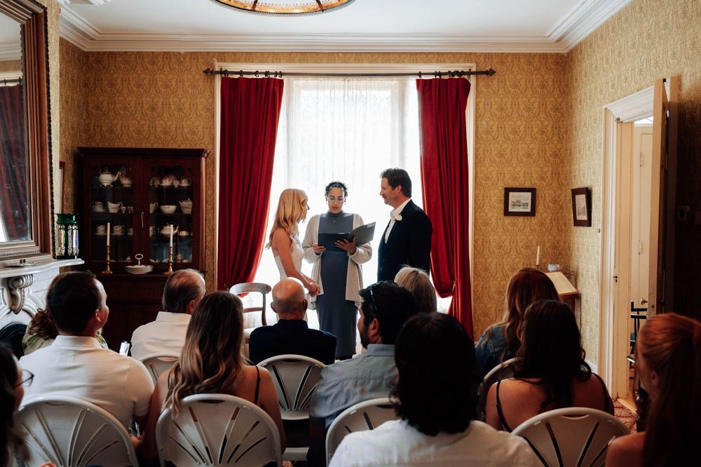 Wedding guests seated in a room with red curtains and ornate decor for an intimate ceremony.