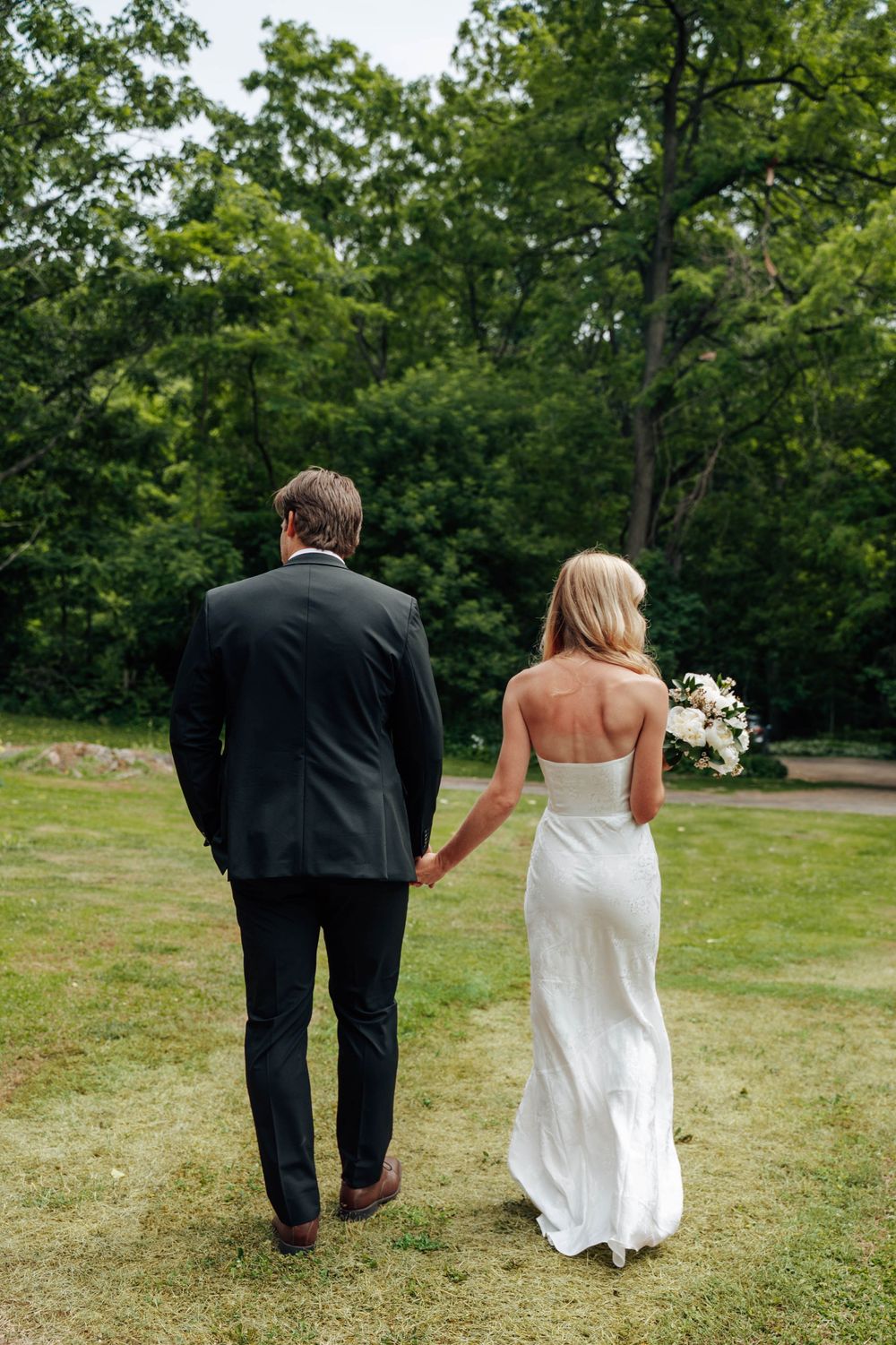Couple walking hand in hand across a green lawn on their wedding day.
