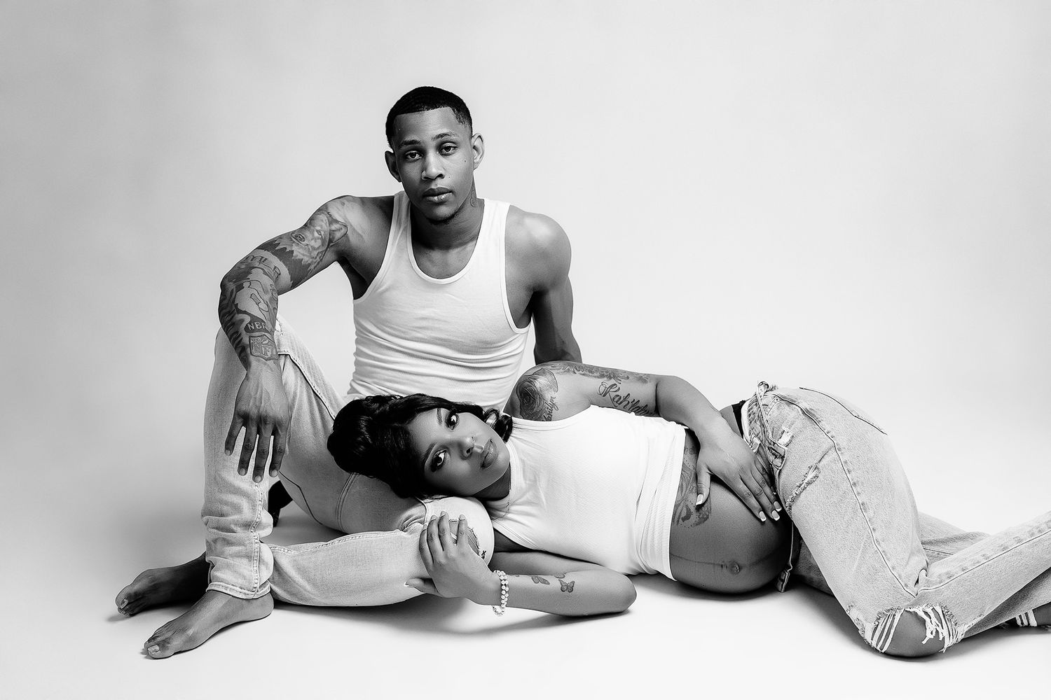 couple posed for studio maternity session on light background. pregnant woman laying head in mans lap.