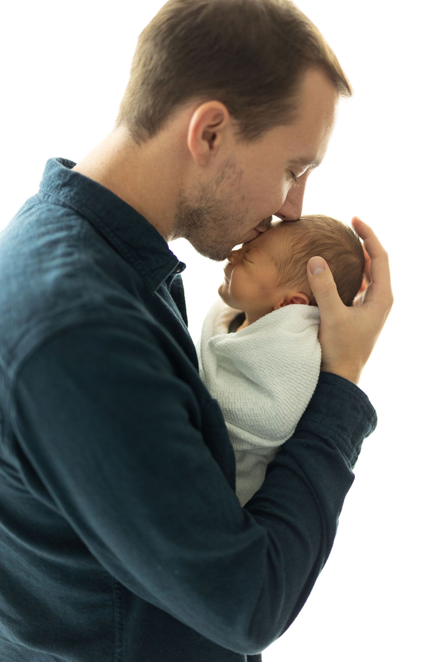 Father kissing newborn son's forehead during an in-home newborn session