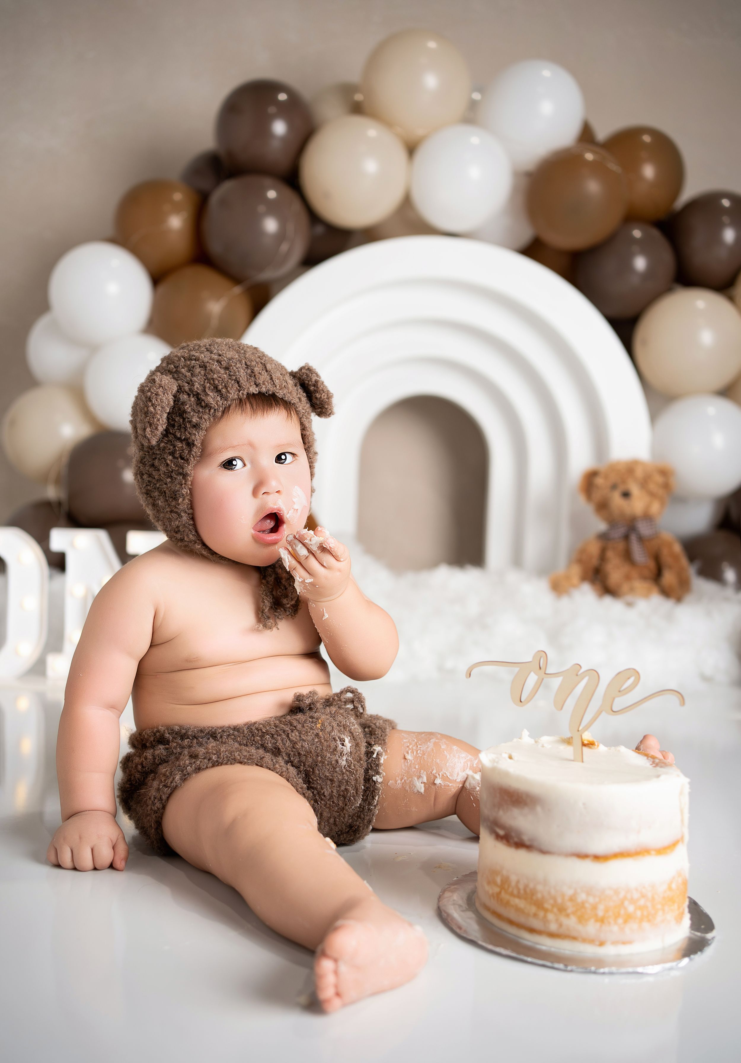 Multiple shots in sequence show a cake smash photo session with brown and white balloon decorations and a simple white cake.