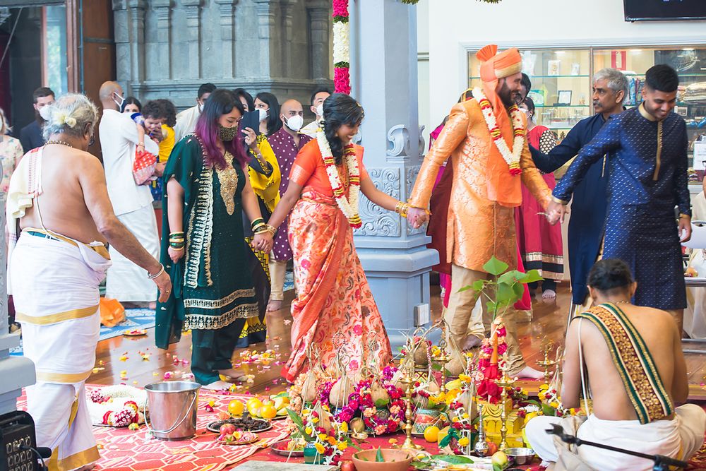 Traditional Hindu wedding ceremony taking place with guests and decorations at an indoor venue.
