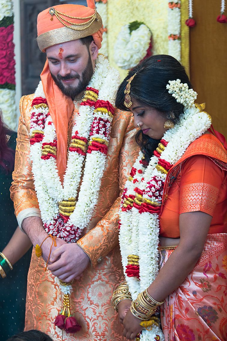 A traditional South Indian wedding ceremony shows the couple exchanging floral garlands during an important ritual moment.