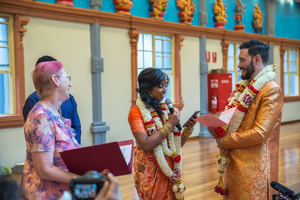 Colorful Hindu wedding ritual with guests in traditional attire participating in ceremonial activities indoors.