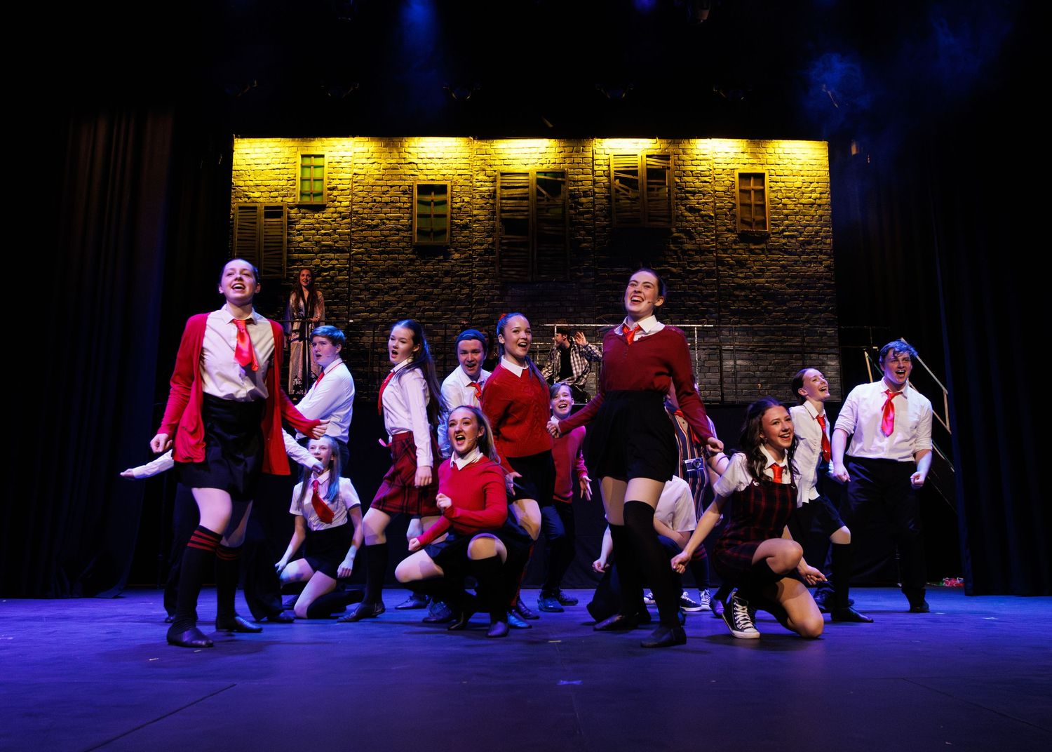 Theater performers in red, black and white costumes strike dramatic poses during a stage musical number.