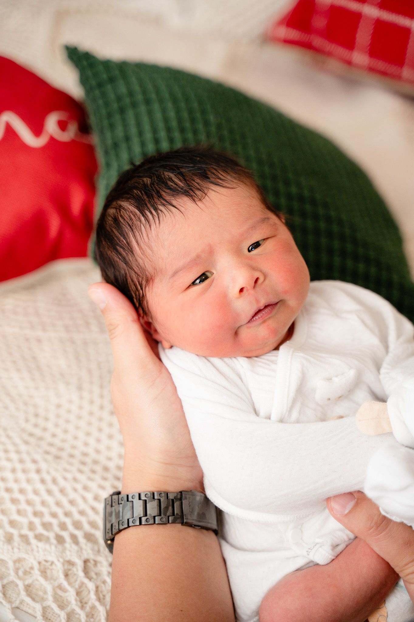 Sweet newborn portrait with red and green pillows against white knit blanket.