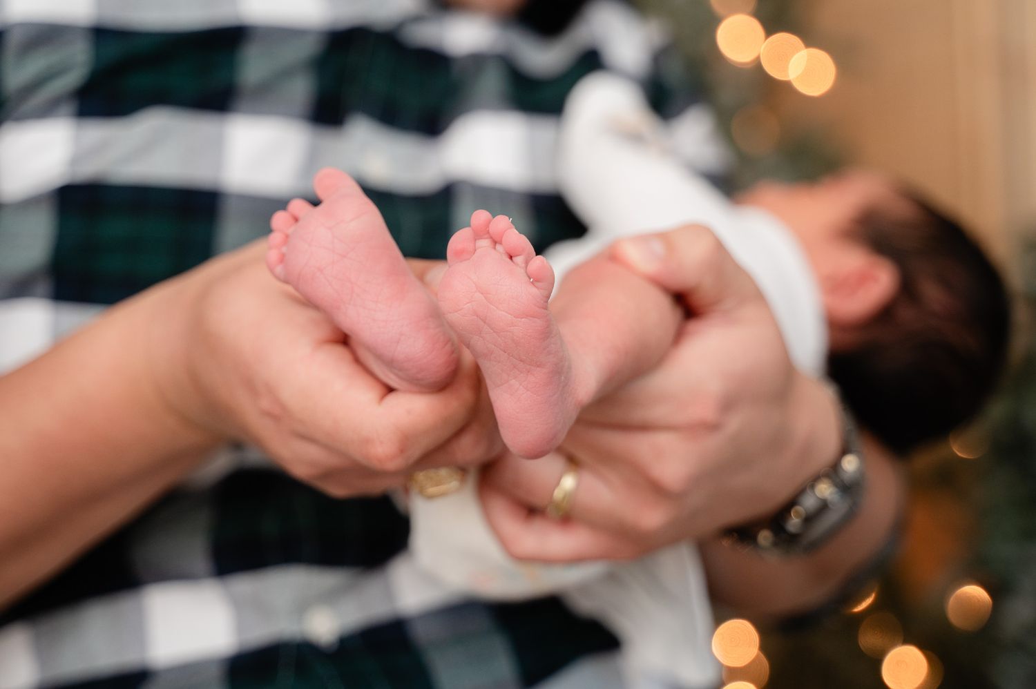 Close up of tiny newborn baby feet being gently held against a plaid background.
