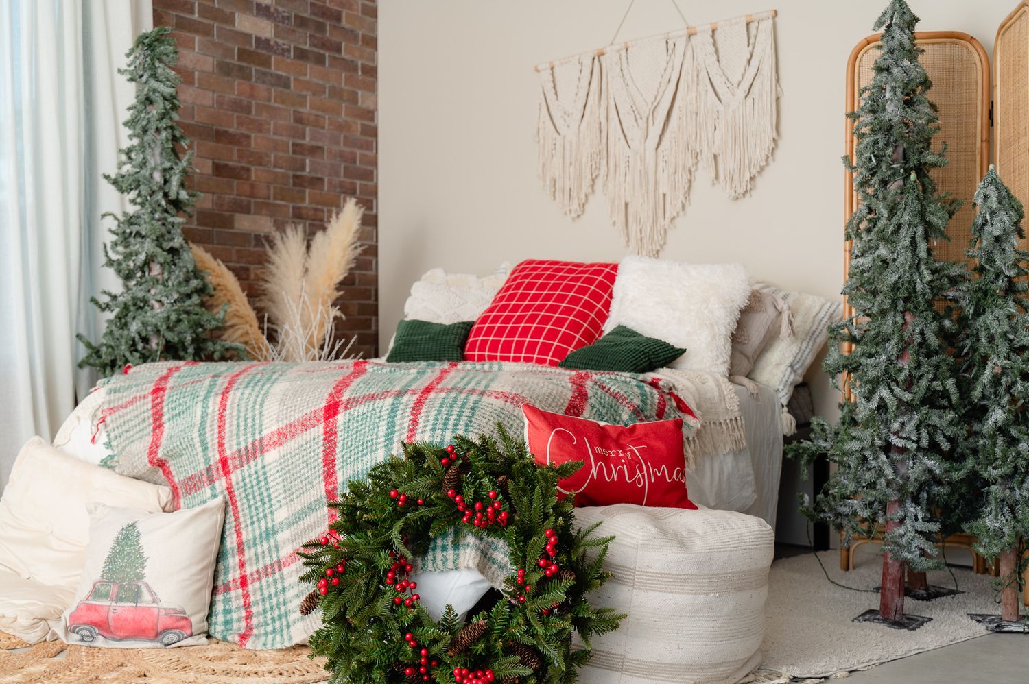 Holiday bedroom setup with artificial trees, wreath and plaid bedding against brick wall.