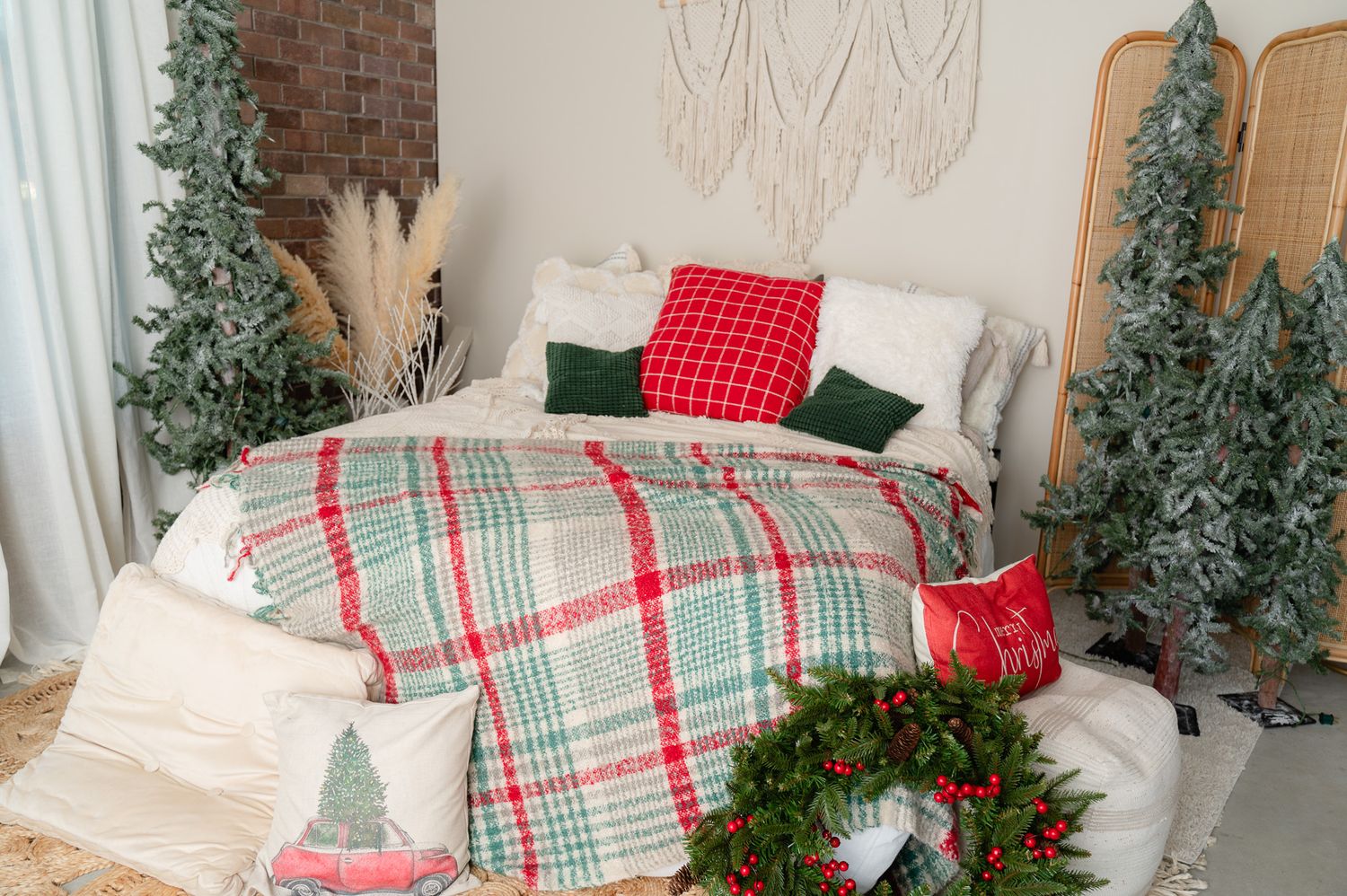 Festive bedroom decor with plaid bedding, Christmas trees and wreaths against exposed brick wall.