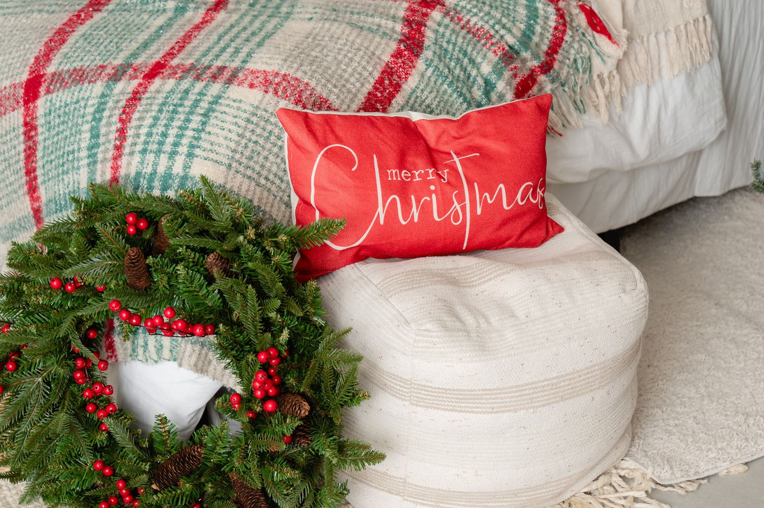 Christmas wreath and plaid throw blanket with holiday pillow on white bedding.
