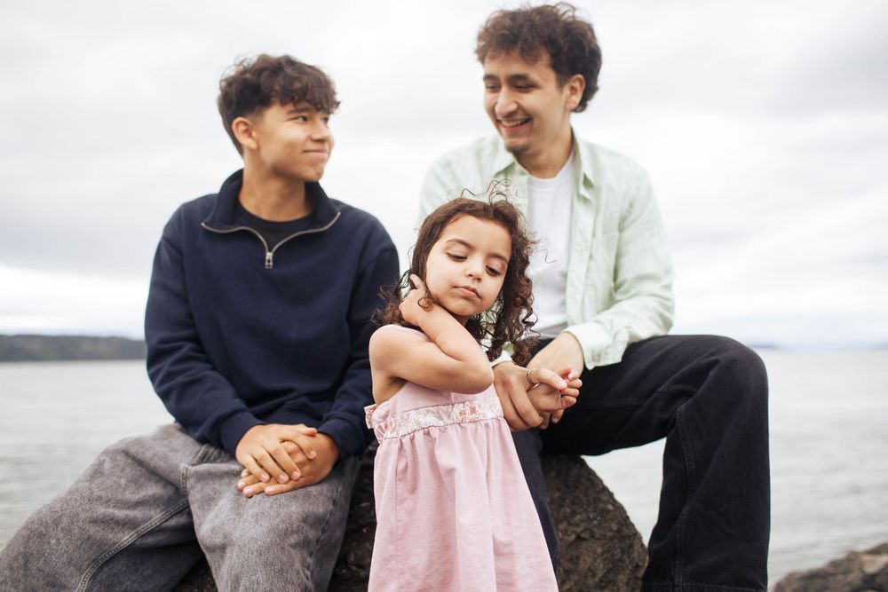 A young girl with her teenage brothers share a loving moment during a family photo session at Mukilteo Beach in Washington