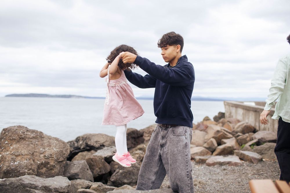 A young girl with her teenage brother share a candid moment of play during a family photo session at Mukilteo Beach in Washington