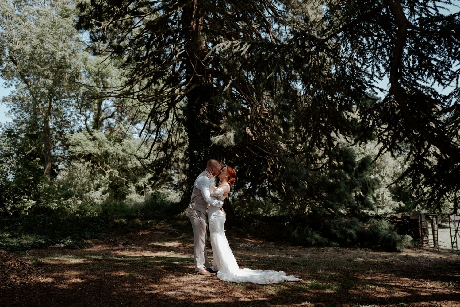 A couple stands in an arched brick doorway with rustic wooden doors opened wide on their wedding day.