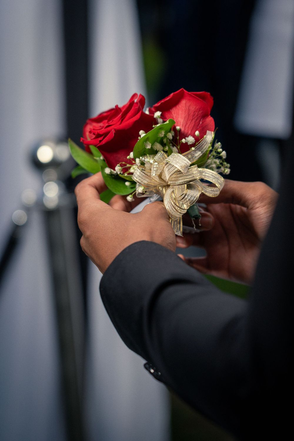 A close-up of hands holding a red rose corsage with gold ribbon and baby's breath flowers.