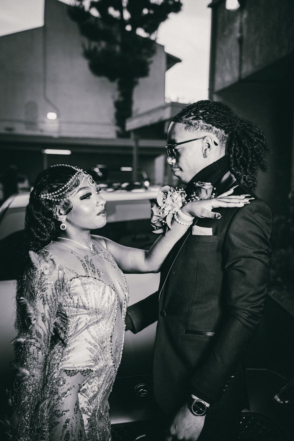 A formal couple shares an intimate moment while adjusting floral accessories before an event.