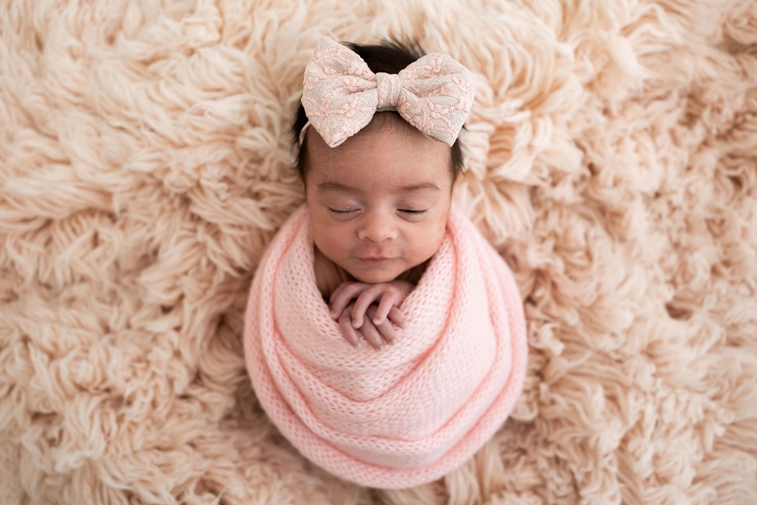 Baby wearing white sweater lying down on soft white fabric in gentle, minimalist nursery setting.