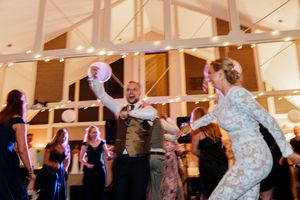 Wedding guests dancing and celebrating on a lively dance floor under string lights at an indoor reception venue.