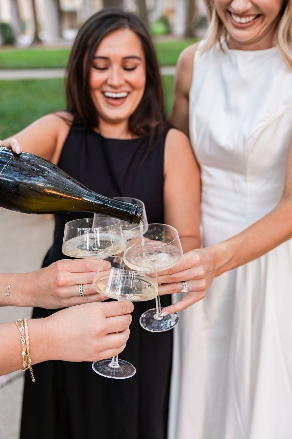 Women laughing as champagne is poured into glasses during outdoor graduation celebration.